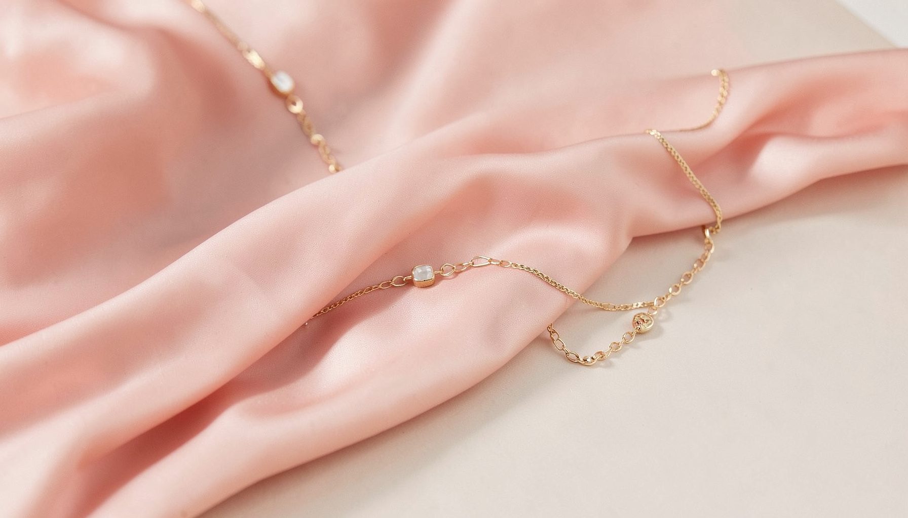 Soft blush-toned fashion editorial scene with flowing fabric and delicate gold jewelry on a neutral backdrop