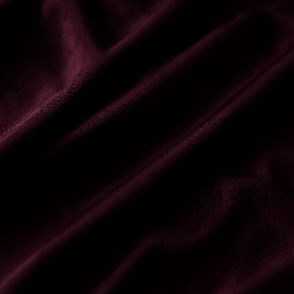 Moody editorial image with deep burgundy and black tones, soft shadows across draped fabric